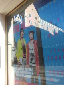 Teatterin sisäänkäynnin esitysjulisteesta heijastuu asiaankuulumattomia kuvia kuten esitykseenkin sulautui aineksien melske.